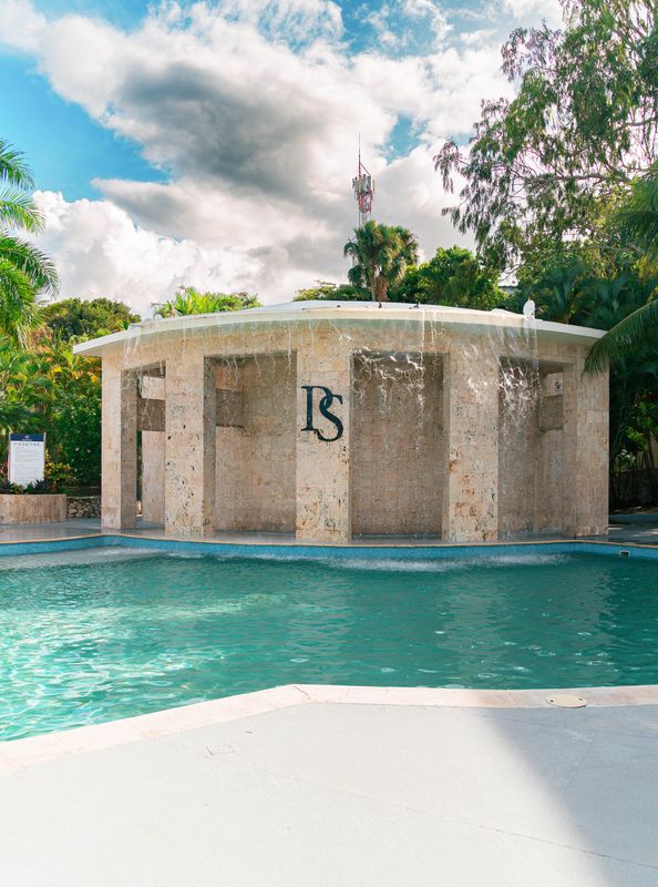 Circular stone waterfall pavilion surrounded by the turquoise water of a resort pool.