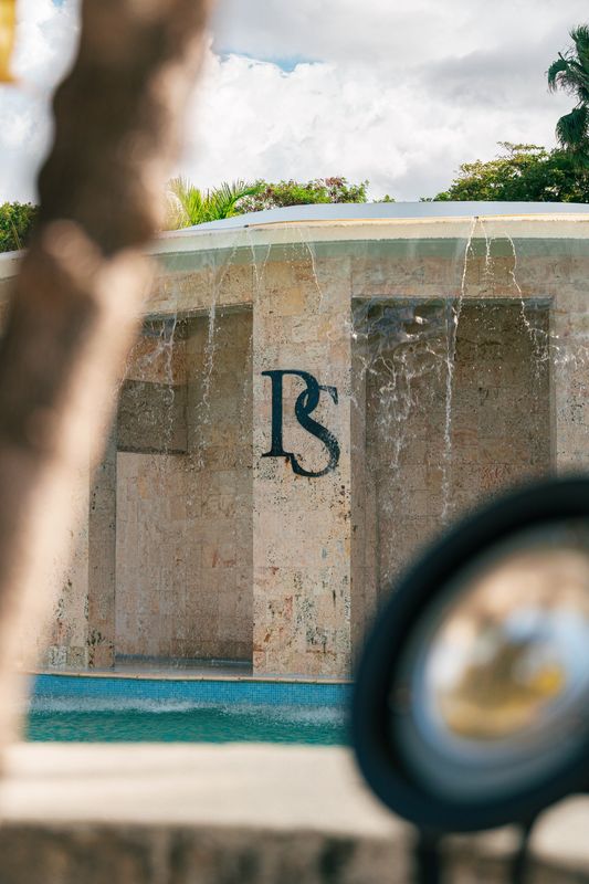 Close view of water cascading over a stone pool pavilion, framed by blurred foreground objects.