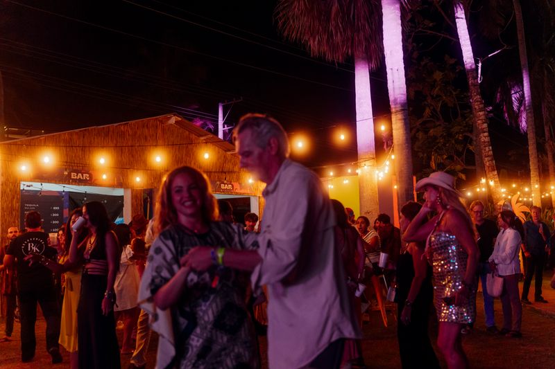 Guests dance outdoors beneath warm string lights during a nighttime festival.