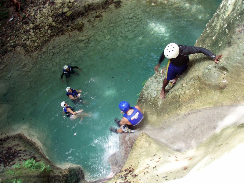 Helmeted visitors gather at a natural waterslide and swimming hole between high rock walls.
