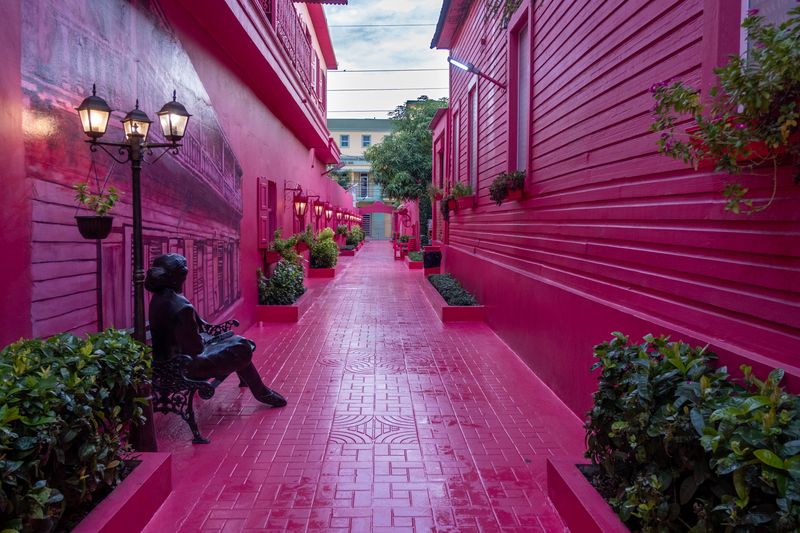 Bright pink pedestrian alley with matching wooden facades, benches, plants and vintage streetlights.